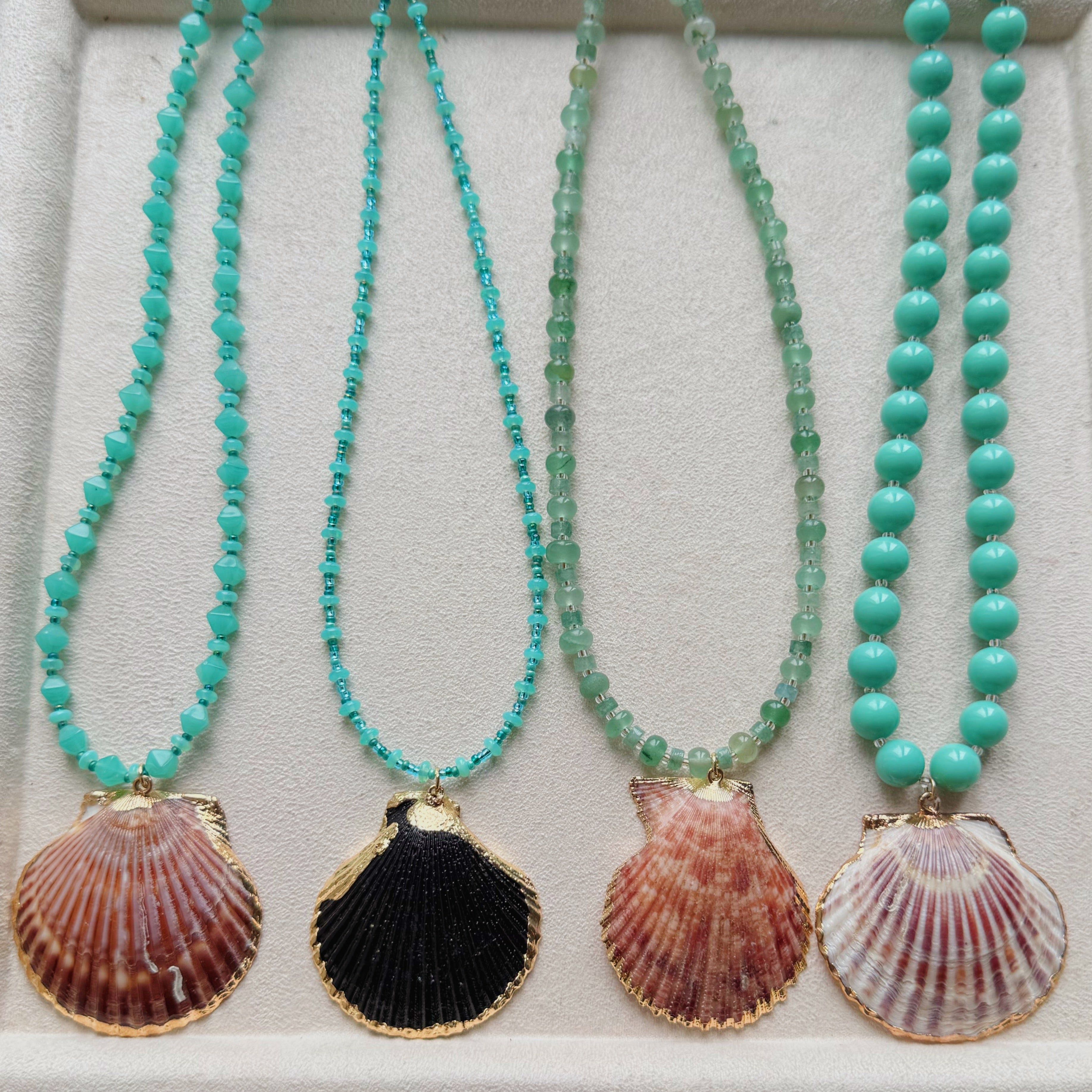 Four turquoise beaded necklaces with shell pendants on a white display tray.