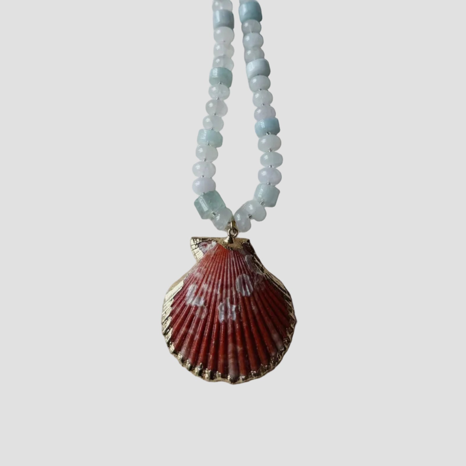 Necklace with a shell pendant and beaded chain on a light gray background